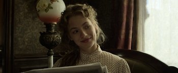 Movie still from “Godless” (2017), directed by Scott Frank – A young woman sitting in front of an old fashioned lamp; Close Up shot, Over the shoulder angle