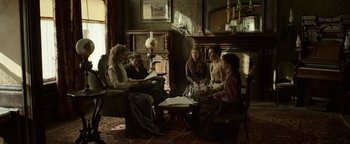Movie still from “Godless” (2017), directed by Scott Frank – A group of people sitting around a living room; Wide shot, High angle