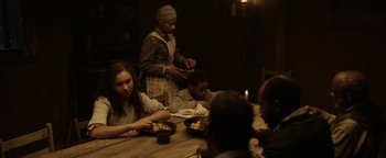 Movie still from “Godless” (2017), directed by Scott Frank – A group of people sitting at a table eating food; Medium shot, Over the shoulder angle