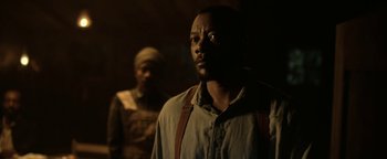 Movie still from “Godless” (2017), directed by Scott Frank – A man standing next to another man in a dark room; Close Up shot, Over the shoulder angle