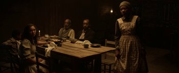 Movie still from “Godless” (2017), directed by Scott Frank – A group of people sitting around a table; Medium shot, Over the shoulder angle