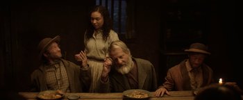 Movie still from “Godless” (2017), directed by Scott Frank – A man sitting at a dinner table with a plate of food in front of him; Medium shot, High angle