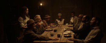 Movie still from “Godless” (2017), directed by Scott Frank – A group of people sitting at a table eating; Medium shot, High angle