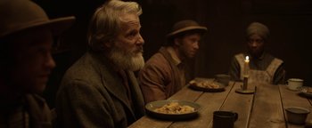 Movie still from “Godless” (2017), directed by Scott Frank – A man sitting at a table with a plate of food; Medium shot, Over the shoulder angle