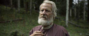 Movie still from “Godless” (2017), directed by Scott Frank – An old man with a beard and a long white beard is holding his hand to his chest; Close Up shot, Over the shoulder angle