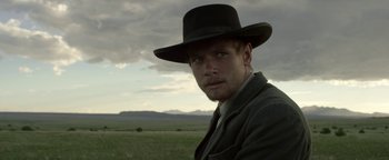 Movie still from “Godless” (2017), directed by Scott Frank – A man in a hat and a suit in a grassy field; Close Up shot, Over the shoulder angle