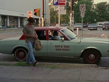 Movie still from “Slacker” (1990), directed by Richard Linklater – A man walking on the sidewalk next to a car; Wide shot, High angle