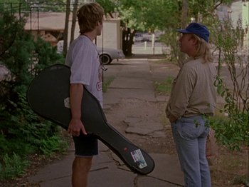 Movie still from “Slacker” (1990), directed by Richard Linklater – A man holding a guitar case talking to a woman; Medium shot, Over the shoulder angle