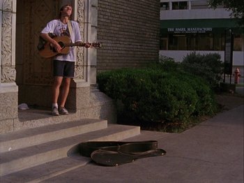 Movie still from “Slacker” (1990), directed by Richard Linklater – A man standing on the steps playing a guitar; Wide shot, Low angle