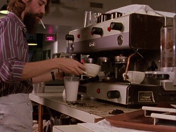 Movie still from “Slacker” (1990), directed by Richard Linklater – A man is making coffee in a coffee shop; Medium shot, High angle