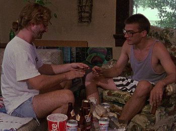 Movie still from “Slacker” (1990), directed by Richard Linklater – Two men sitting on the ground with beer and cigarettes; Medium shot, Low angle