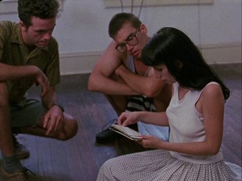 Movie still from “Slacker” (1990), directed by Richard Linklater – A group of people sitting on the floor looking at a book; Medium shot, Over the shoulder angle
