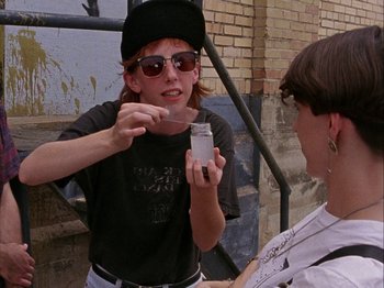 Movie still from “Slacker” (1990), directed by Richard Linklater – A person holding a container in one hand and a spoon in the other hand; Medium shot, Over the shoulder angle