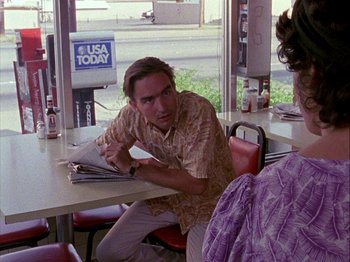 Movie still from “Slacker” (1990), directed by Richard Linklater – A man sitting at a table in front of a woman; Medium shot, Over the shoulder angle
