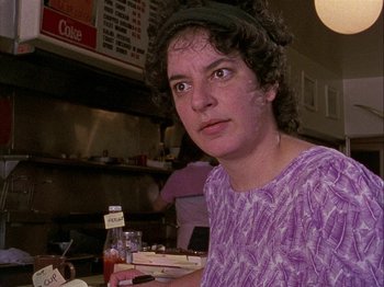 Movie still from “Slacker” (1990), directed by Richard Linklater – A woman in a purple shirt holding a box of food; Close Up shot, Low angle