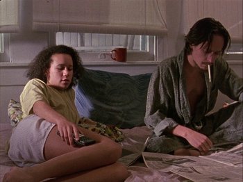 Movie still from “Slacker” (1990), directed by Richard Linklater – Two people sitting on a bed and one is smoking a cigarette and the other is holding a remote control; Medium shot, Low angle
