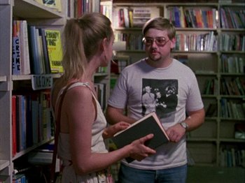 Movie still from “Slacker” (1990), directed by Richard Linklater – A man and a woman standing next to each other in a library; Medium shot, Over the shoulder angle