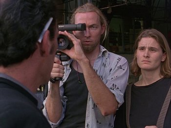 Movie still from “Slacker” (1990), directed by Richard Linklater – A man with long blonde hair is holding a video camera; Close Up shot, Over the shoulder angle