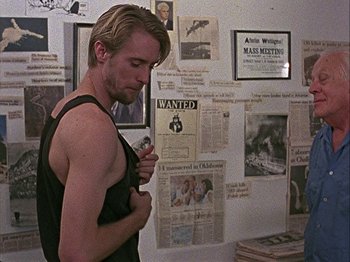 Movie still from “Slacker” (1990), directed by Richard Linklater – A man standing in front of a wall covered with papers; Medium shot, Over the shoulder angle