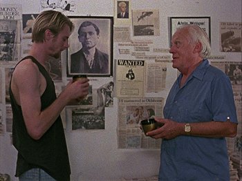 Movie still from “Slacker” (1990), directed by Richard Linklater – Two men standing in front of a wall with pictures on it; Medium shot, Over the shoulder angle