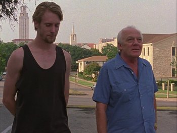 Movie still from “Slacker” (1990), directed by Richard Linklater – A man standing next to another man on a city street; Medium shot, Low angle