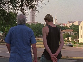 Movie still from “Slacker” (1990), directed by Richard Linklater – A man and a woman standing next to each other on the side of a road; Medium shot, Low angle