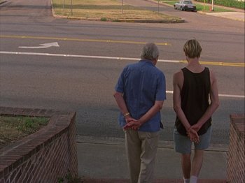 Movie still from “Slacker” (1990), directed by Richard Linklater – A man and a woman standing next to each other on the side of the road; Wide shot, Low angle