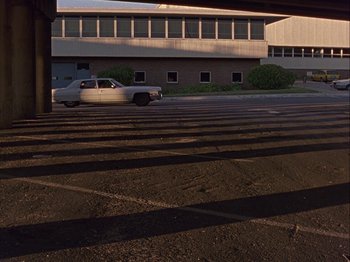 Movie still from “Slacker” (1990), directed by Richard Linklater – A white truck parked in a parking lot near a building; Extreme Wide shot, High angle