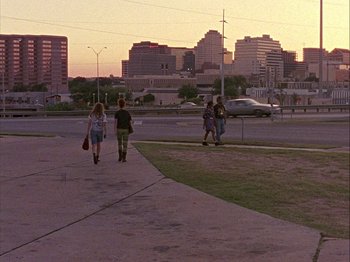 Movie still from “Slacker” (1990), directed by Richard Linklater – A group of people walking down a sidewalk near a street; Extreme Wide shot, Low angle