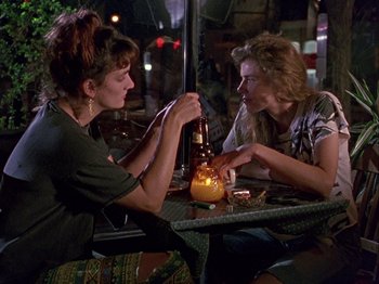 Movie still from “Slacker” (1990), directed by Richard Linklater – Two people sitting at a table with a bottle of beer; Medium shot, Over the shoulder angle