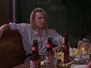 Movie still from “Slacker” (1990), directed by Richard Linklater – A woman sitting at a table with several bottles of beer; Medium shot, Over the shoulder angle