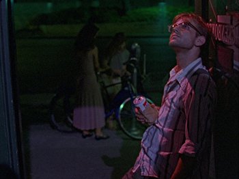 Movie still from “Slacker” (1990), directed by Richard Linklater – A man holding a cell phone while standing next to a bicycle; Medium shot, Low angle
