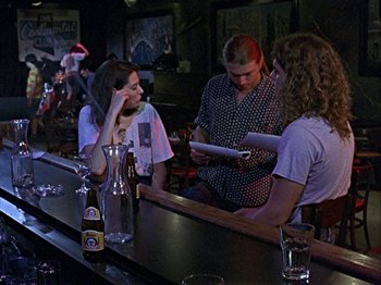 Movie still from “Slacker” (1990), directed by Richard Linklater – A group of people sitting at a bar looking at papers; Medium shot, Over the shoulder angle