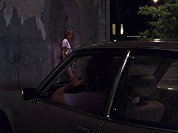 Movie still from “Slacker” (1990), directed by Richard Linklater – A person standing in a parked car with a cat on the back of the car; Wide shot, Over the shoulder angle