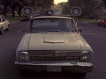 Movie still from “Slacker” (1990), directed by Richard Linklater – An old car is parked on the side of the road; Wide shot, Low angle