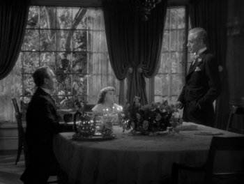 Movie still from “Smilin' Through” (1932), directed by Sidney Franklin – A black and white photo of a man and a woman sitting at a table; Medium shot, High angle