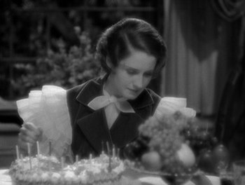Movie still from “Smilin' Through” (1932), directed by Sidney Franklin – A woman sitting at a dinner table looking at a cake; Close Up shot, High angle