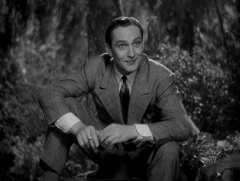 Movie still from “Smilin' Through” (1932), directed by Sidney Franklin – A man in a suit sitting on the ground in front of trees; Medium shot, Low angle