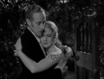 Movie still from “Smilin' Through” (1932), directed by Sidney Franklin – A man and a woman embracing each other in front of a fence; Medium shot, High angle