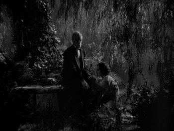 Movie still from “Smilin' Through” (1932), directed by Sidney Franklin – Two people sitting on a bench near a body of water; Wide shot, High angle