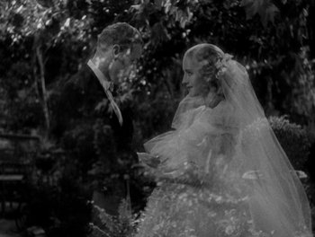 Movie still from “Smilin' Through” (1932), directed by Sidney Franklin – A man and a woman standing next to each other in front of a tree; Medium shot, High angle