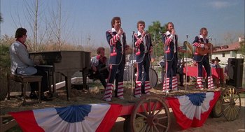 Movie still from “Smokey and the Bandit II” (1980), directed by Hal Needham – A group of men standing on top of a stage singing; Wide shot, High angle