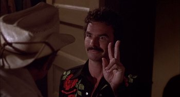 Movie still from “Smokey and the Bandit II” (1980), directed by Hal Needham – A man with a beard and a mustache giving the peace sign with one hand; Close Up shot, Over the shoulder angle