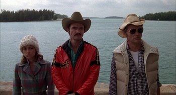 Movie still from “Smokey and the Bandit II” (1980), directed by Hal Needham – A group of men standing next to each other near a body of water; Medium shot, Over the shoulder angle