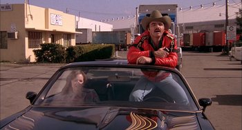 Movie still from “Smokey and the Bandit II” (1980), directed by Hal Needham – A man in a cowboy hat sitting on the hood of a car; Medium shot, Low angle