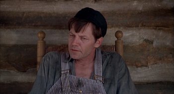 Movie still from “Smokey and the Bandit II” (1980), directed by Hal Needham – A man sitting in a chair wearing an overalls and a hat; Close Up shot, High angle