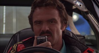 Movie still from “Smokey and the Bandit II” (1980), directed by Hal Needham – A man in a car holding a cell phone to his mouth; Close Up shot, Low angle