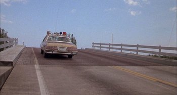 Movie still from “Smokey and the Bandit II” (1980), directed by Hal Needham – An old car driving down a road with a white fence; Wide shot, Low angle