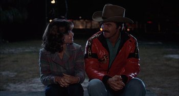 Movie still from “Smokey and the Bandit II” (1980), directed by Hal Needham – A man and a woman sitting next to each other on the ground; Medium shot, Over the shoulder angle