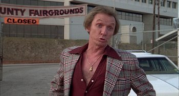 Movie still from “Smokey and the Bandit II” (1980), directed by Hal Needham – A man in a plaid jacket standing in a parking lot; Medium shot, Low angle